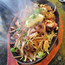 A steaming dish of food on an iron skillet