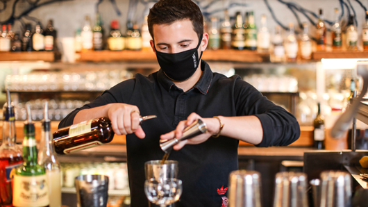 A bartender with a mask on making a cocktail