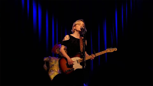Lydia Loveless singing with a guitar in front of a crowd