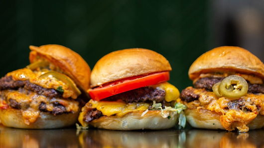 Three cheeseburger sliders with cheddar cheese, jalapeno peppers and more
