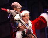 Ira David Wood III stars at Scrooge in the hit holiday comedy A Christmas Carol; photo is taken of Scrooge holding a small boy and both holding arms in the air as if celebrating something