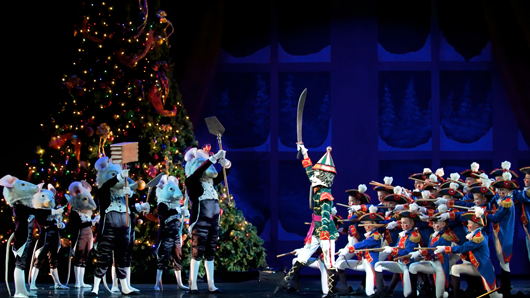 A scene in The Nutcracker with an army of mice fighting an army of toy soldiers in front of a Christmas tree
