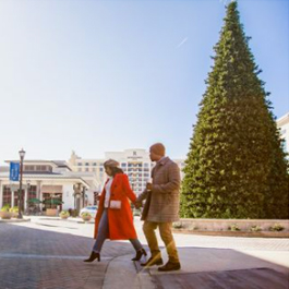 A couple walking in front of a holiday tree with a large hotel in the background
