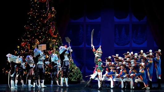 Scene from The Nutcracker ballet with toy soldiers battling rat people in front of a giant Christmas tree