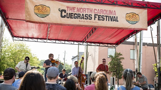 Festival stage with four musicians playing instruments in front of standing crowd