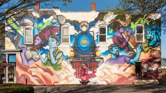 A vibrant, colorful mural of a train, with artists surrounding it