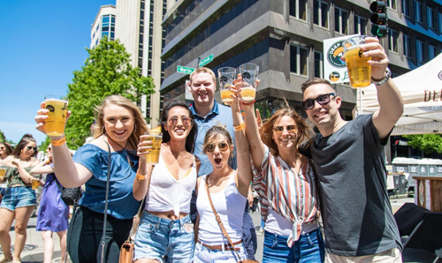 A group of friends raising a toast with beers at the outdoor Brewgaloo event in downtown Raleigh