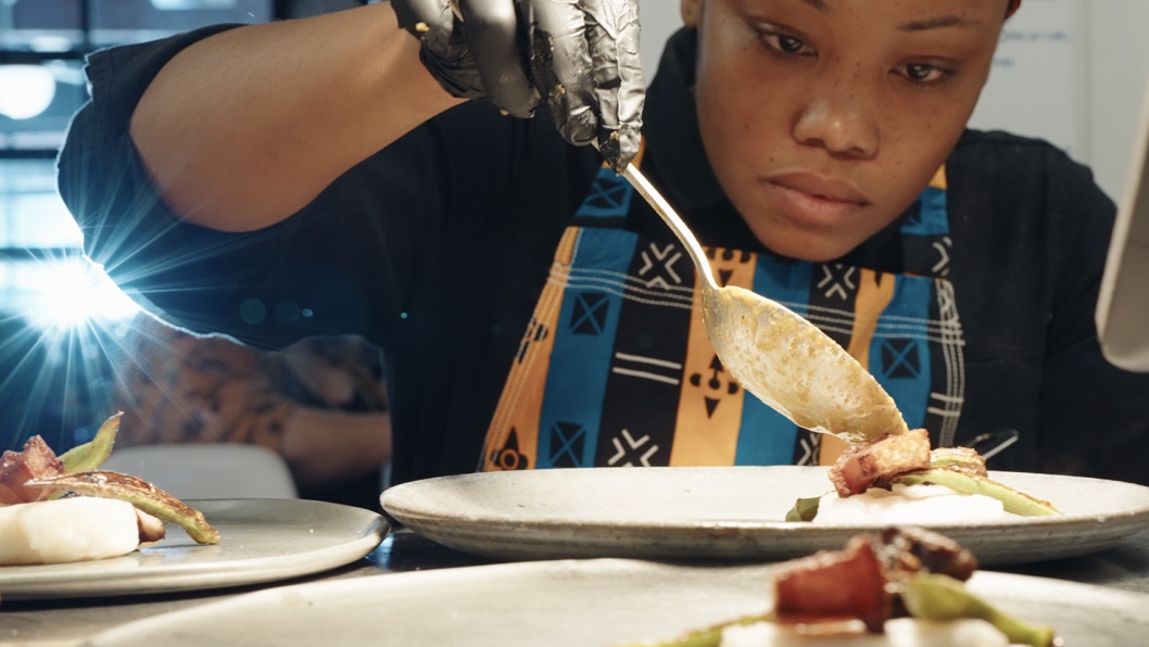 Chef Adé Carrena focuses on plating a menu item with a spoon. 