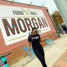 A woman smiling in front of a large Morgan Street Food Hall mural