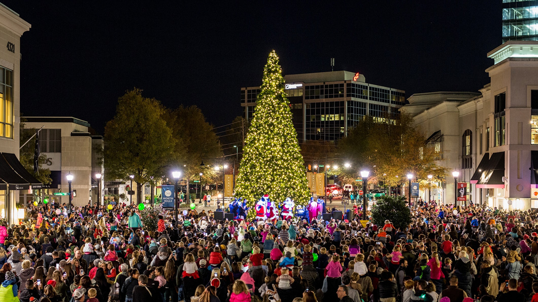 Nighttime crowd gathers around 40-foot-tall Christmas Tree in the middle of the North Hills shopping district. Santa cheers as the tree has just been lit. 