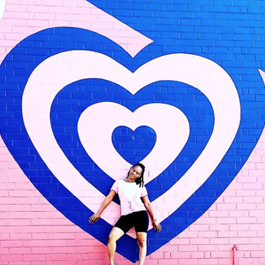 Woman in front of a giant pink and blue heart mural