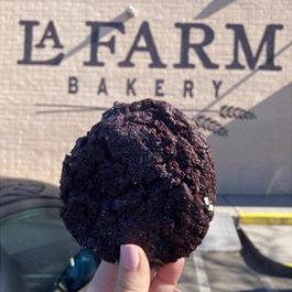 Chocolate chip cookie being held up in front of a La Farm Bakery logo mural