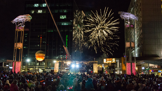 A nighttime crowd gathers in Raleigh's City Plaza as the Raleigh Acorn falls at midnight and fireworks go off in the background