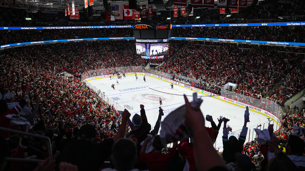 A wide shot from the corner of a fully packed PNC Arena, with a crowd cheering with arms in the air for the Carolina Hurricanes