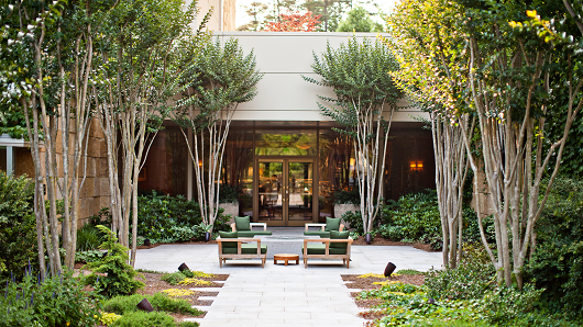 A serene courtyard in Umstead Hotel with trees and green chairs and a table in a round, paved area