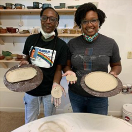 Two women holding out clay trays