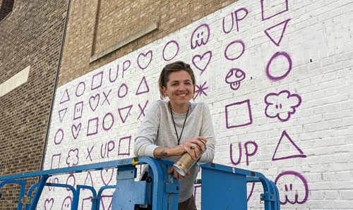 Artist Taylor White on a lift next to a large mural she worked on