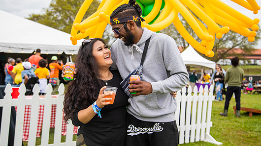A couple laughing and smiling at each other outside a food and beverage tent at a festival