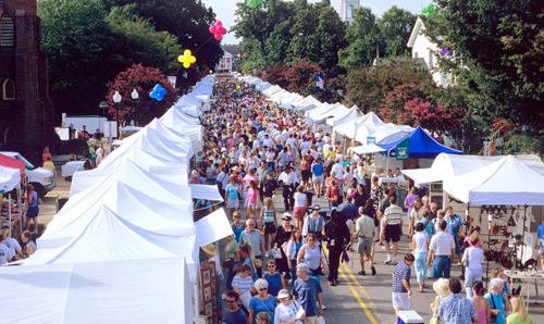 A crowd at a small-town festival with tents lining the street