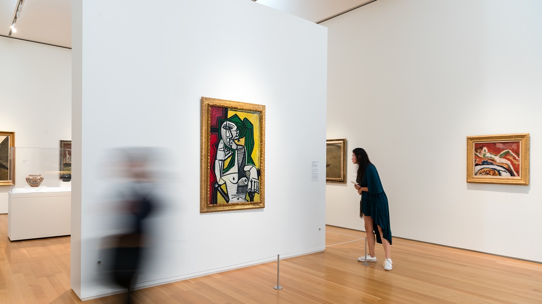 A Pablo Picasso painting, "Seated Woman, Red and Yellow Background (Femme assise, fond rouge et jaune)", hangs on a gallery wall all by itself at the North Carolina Museum of Art as a visitor moves in for a closer look.