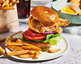 Chicken sandwich stacked high with a big piece of fried chicken, tomatoes, lettuce, onions and other fixings