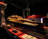 A dimly lit exhibit room within a museum, with a model of a shipwreck displayed within a well-lit case