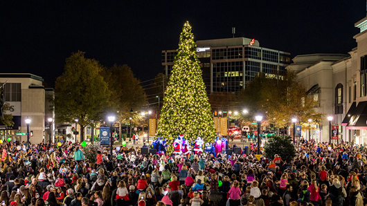 Nighttime crowd gathers around 40-foot-tall Christmas Tree in the middle of the North Hills shopping district. Santa cheers as the tree has just been lit. 