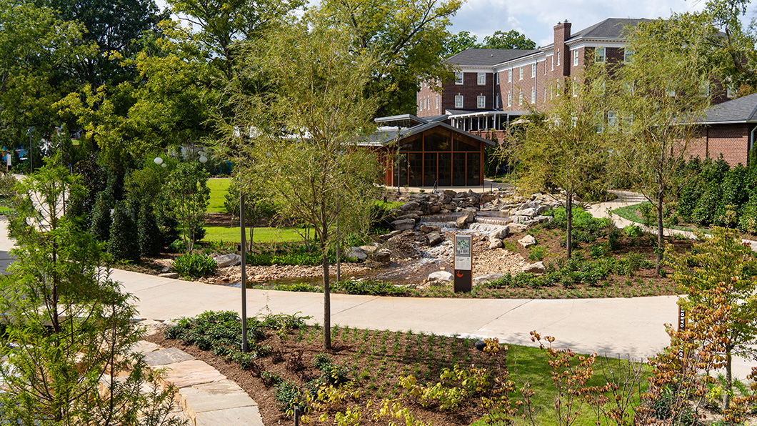 Downtown Cary Park is filled with new trees and plants; paved walkways cut through the middle of the park; an event space, The Gathering House, sits in the background on a sunny day