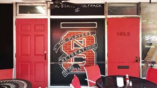 The front door to Players' Retreat, with a large North Carolina State University logo in red and black and a sign that reads 'Est. 1951'