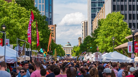 A view looking over a crowd towards the North Carolina State Capitol on Fayetteville St. in downtown Raleigh, with vendor tents lining the street and people enjoying a sunny day in spring