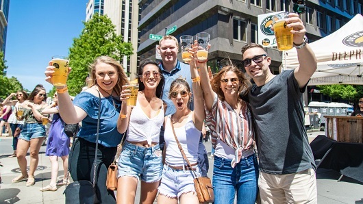 A group of friends raising a glass of beer on a downtown Raleigh street during Brewgaloo craft beer festival