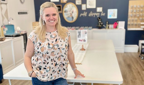 A smiling woman standing in front of a work table in a stylishly decorated workshop