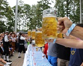 An Oktoberfest celebration with participants holding out giant mugs filled with beer, ready for a signal to start drinking quickly while a large crowd cheers them on