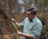 Daniel Woody examines a long, green leaf he is holding somewhere outdoors
