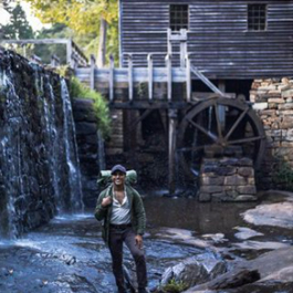 Man standing in front of a historic gristmill with a pond below it