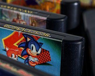 A video game cartridge featuring Sonic the Hedgehog is pictured in focus, with other games out of focus in the foreground and background.