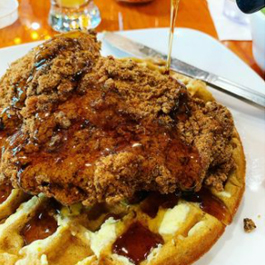 A platter of chicken and waffles with syrup poured over