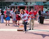A woman in a Carolina Hurricanes hockey jersey playing a game of bag toss; a small crowd congregates behind her