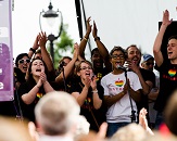Diverse group of young adults on stage singing and clapping with hands in the air in front of crowd