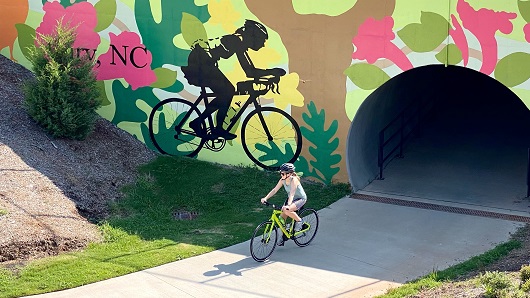 Cyclist comes out of tunnel in front of bicycle mural on paved Cary greenway