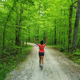 A woman running through a wooded trail with her hands up