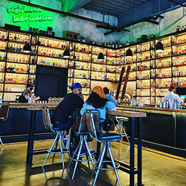 A couple sitting in the middle of a bar with lots of liquor bottles lining the walls, floor to ceiling
