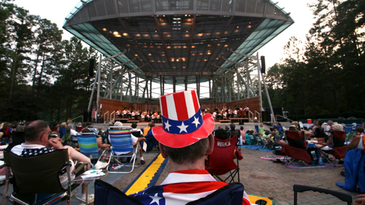 Man with a patriotic, American flag hat watching a concert at an outdoor amphitheater