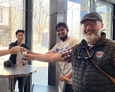 Greg Whitt—a white man approximately 50 years old, wearing a plaid shirt, vest and cap—holds up a tasting cup of coffee with his tour participants at a downtown Raleigh coffee shop