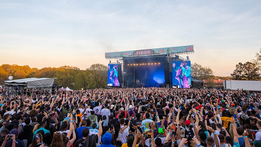 A large crowd with their hands up in front of a large, outdoor stage at Dreamville Festival
