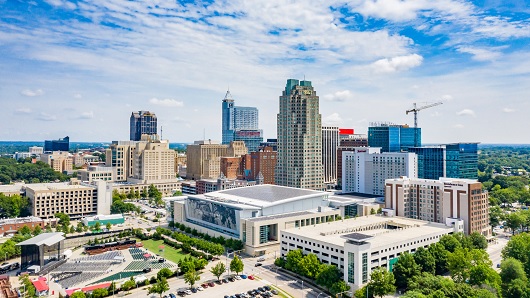 A drone view of the downtown Raleigh skyline looking north over the Raleigh Convention Center on a sunny day with very blue skies