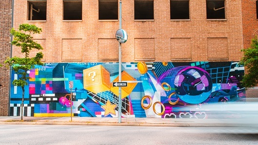 Colorful video game mural with rings, question-mark cubes, stars and more on the side of a brick parking lot wall