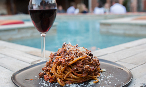 Close-up photo of a plate of spaghetti next to a glass of wine